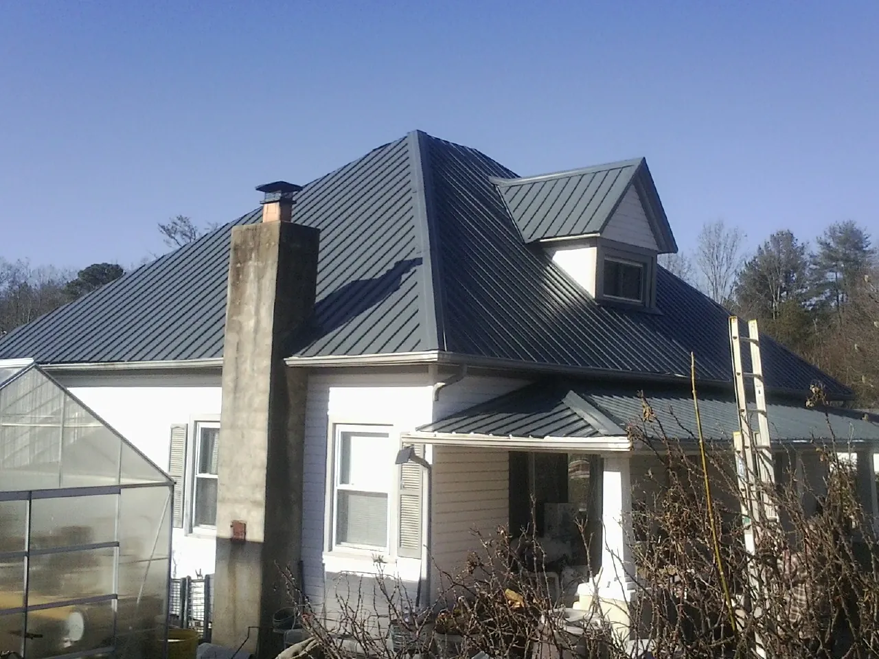 Dark blue standing seam metal roof on a white farmhouse with dormer — Slate & Tile Roof Repair by Roofing Brothers in Brookeville