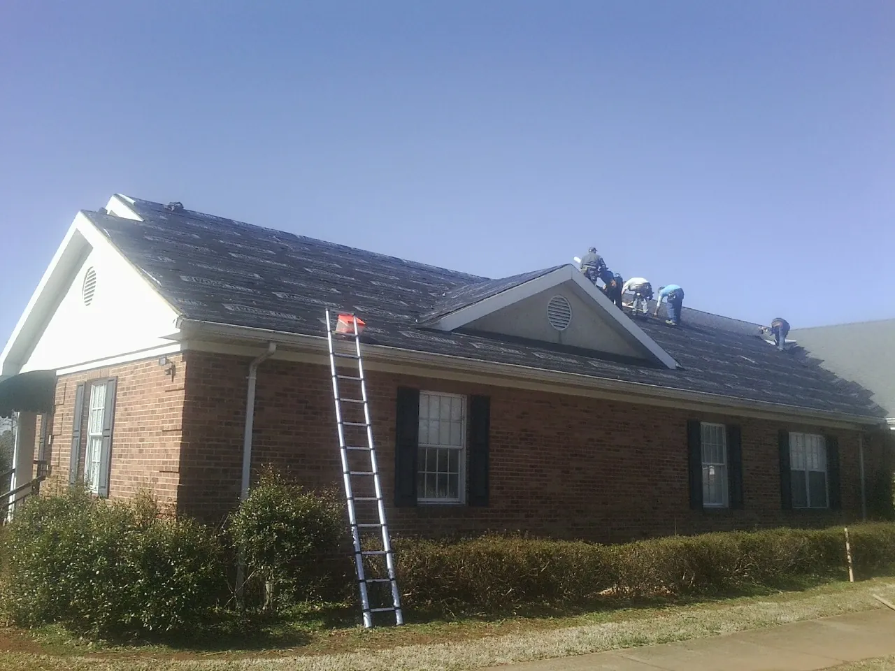 Crew tearing shingles off a brick ranch roof with a ladder set — Emergency Roof Repair work by our crew in Brookeville