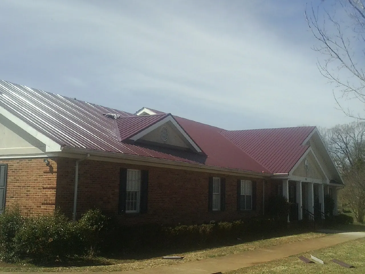 Red metal roof with gabled entries on a long brick building, from a Hail Damage Roof Repair job in Brookeville
