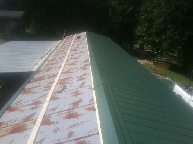 Old rusted panels beside newly installed green metal roofing — Wind Damage Roof Repair by Roofing Brothers in Brookeville