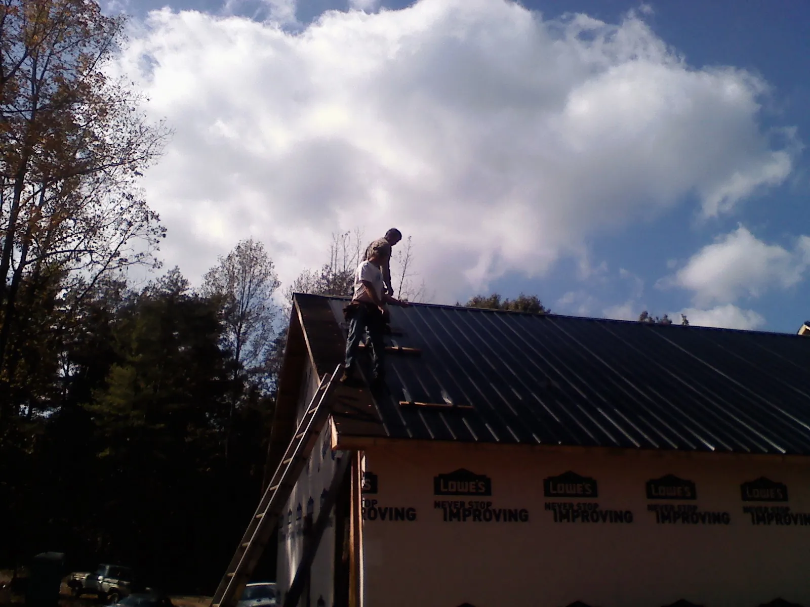 Roofer fastening dark metal panels high against a cloudy sky, from a Roof Inspection job in Brookeville