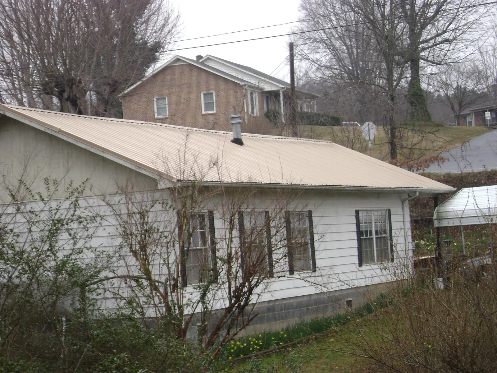 Tan metal roof on a white sided house set into a hillside — Commercial Roofing by Roofing Brothers in Brookeville