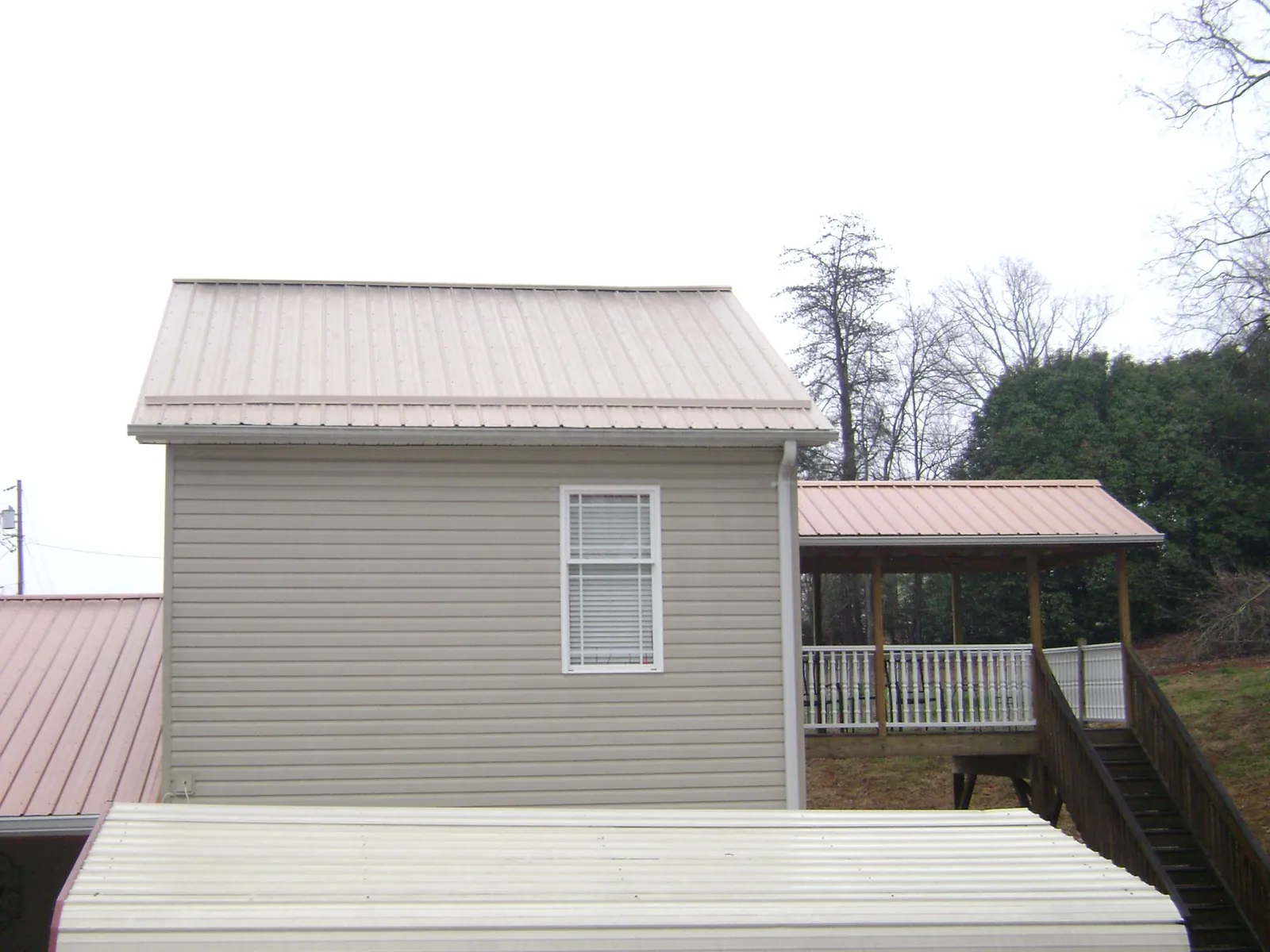 Tan metal roofs on a two story addition and attached porch, from a Roof Replacement job in Brookeville